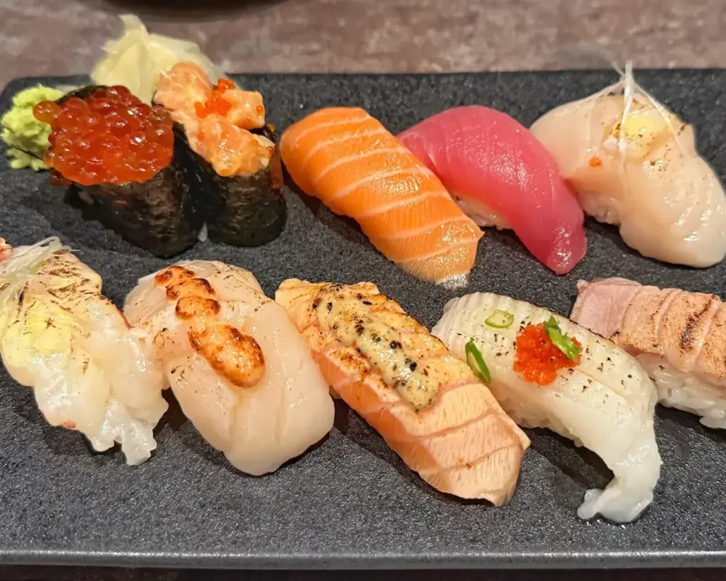 A beautifully arranged plate featuring assorted sushi, including nigiri and rolls, with fresh fish slices, rice, and garnishes presented in an elegant dining setting.