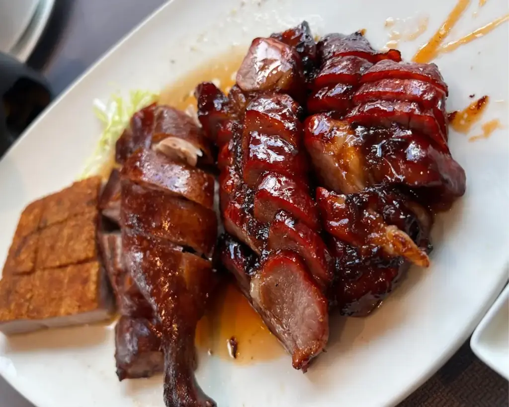 A plate of roasted Peking duck with crispy golden-brown skin and tender meat, sliced neatly and served with traditional accompaniments.