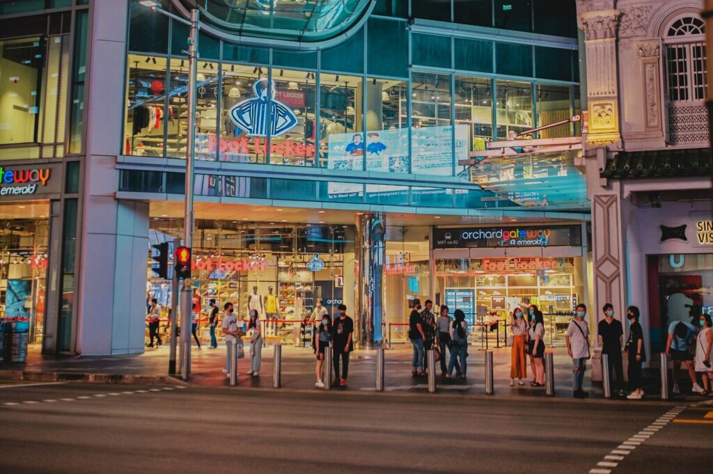 A group of people gathered outside a store on Orchard Road, Singapore, illuminated by night lights.