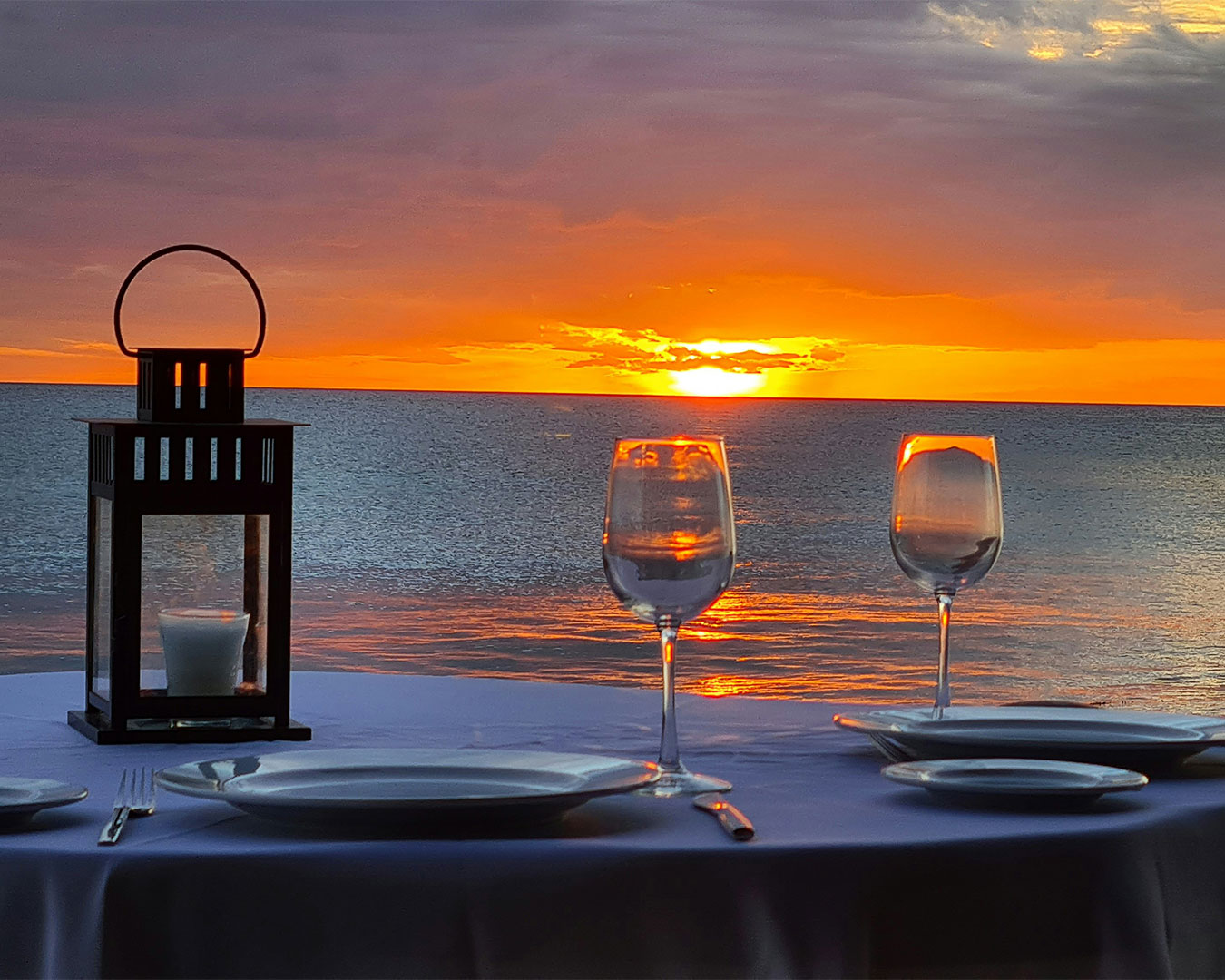A neatly arranged glass and plate set on a dining table by the window, with warm sunset light casting a soft glow across the table and creating a calm, elegant dining atmosphere.