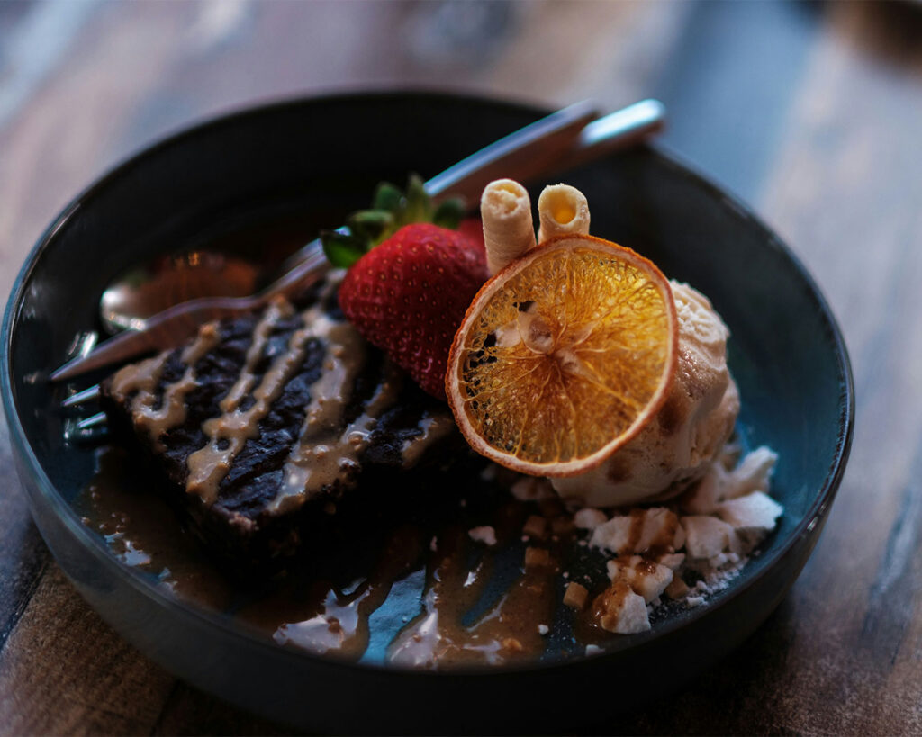A plate of warm brownies topped with a scoop of vanilla ice cream, served at a café with a relaxed and inviting setting.