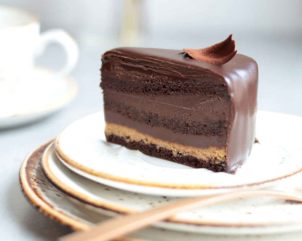 Close-up view of a thick slice of chocolate cake with layered sponge and creamy chocolate frosting, presented neatly on a plate for an indulgent dessert focus.