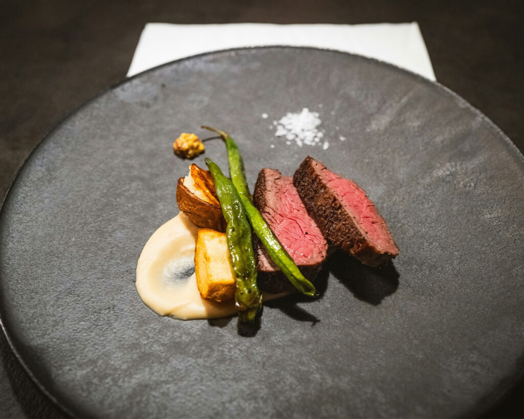 A beautifully plated meat entrée with tender slices of meat, complemented by rich sauce and carefully arranged sides, served on a modern plate for an upscale fine-dining presentation.
