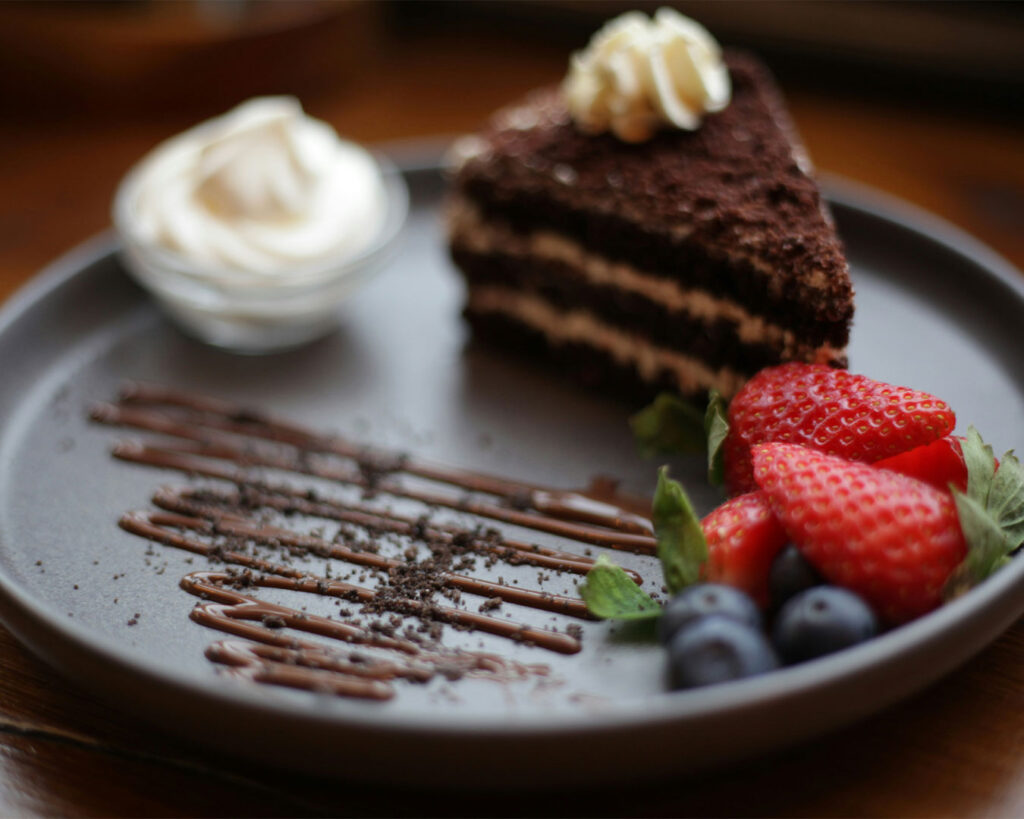 A decadent slice of chocolate cake on a white plate, with rich layers and a glossy chocolate topping, tempting and indulgent.