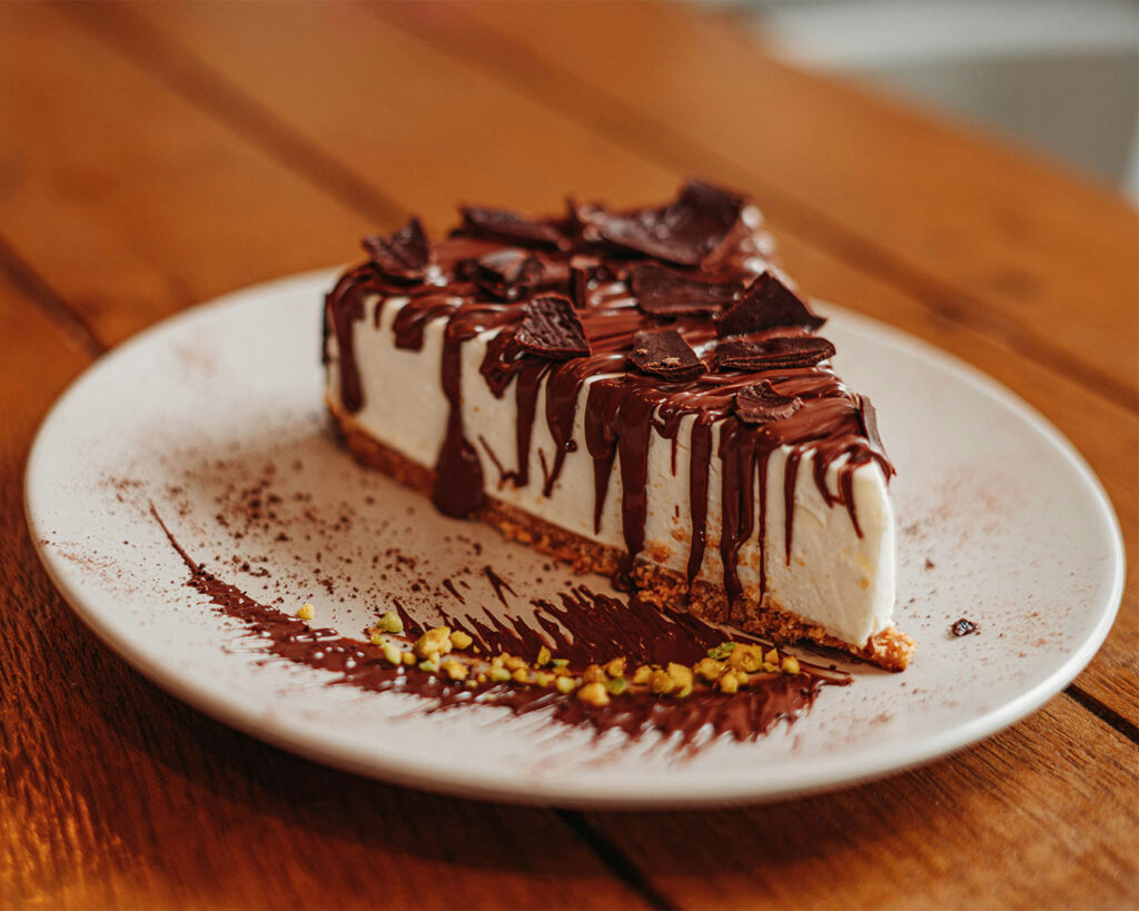 A single slice of rich chocolate cheesecake on a dessert plate, with smooth texture and decorative drizzle on top.