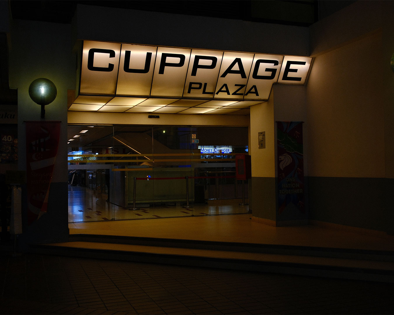 The exterior of Cuppage Plaza, a multi-storey building along a busy Orchard Road street, with visible shop signs and passing traffic, showing the lively atmosphere of Singapore’s dining and nightlife area.