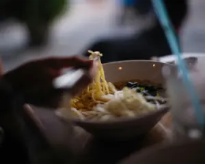 Close-up of chopsticks lifting a portion of noodles from a bowl, showing the texture from the freshly prepared dish
