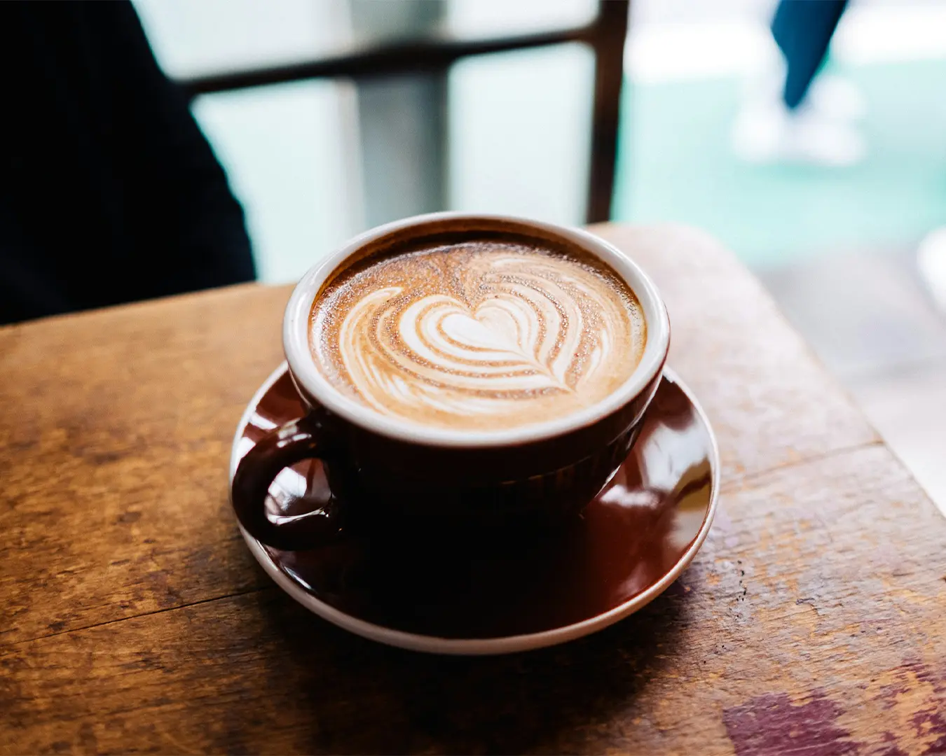 A freshly brewed cup of coffee topped with delicate latte art, featuring a smooth, creamy foam pattern swirling across the surface.