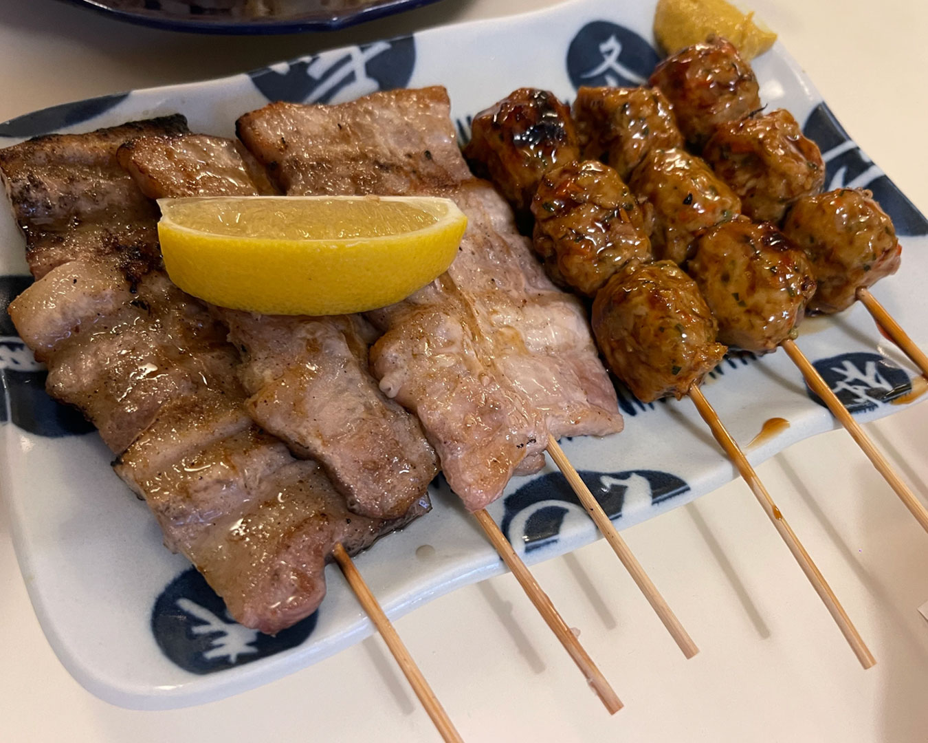 A grilled chicken skewer served on a small plate, with lightly charred edges and a glossy glaze, presented in a warm-lit izakaya setting that highlights its freshly grilled texture.