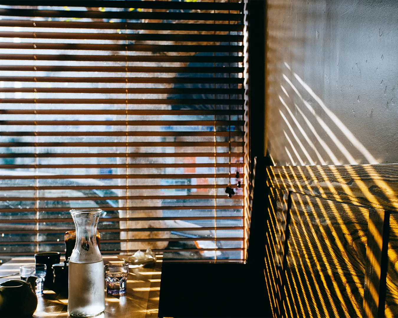 A cosy restaurant seating area beside large windows, where warm sunlight pours in and softly lights the wooden tables and chairs, creating a calm and welcoming daytime dining ambience.