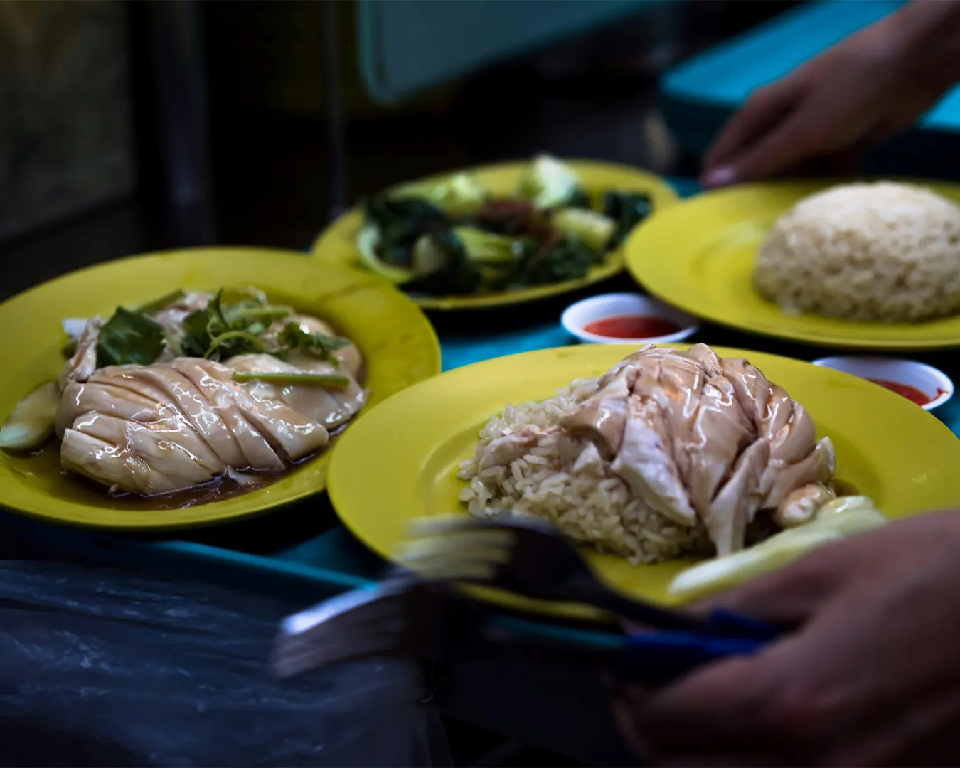 A plate of fragrant Hainanese chicken rice featuring tender poached chicken slices over aromatic rice, served with chilli sauce, ginger paste, and dark soy sauce.