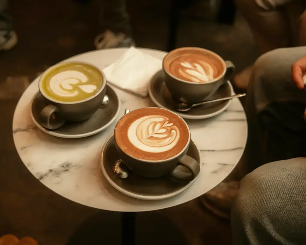 Three freshly prepared cups of coffee placed neatly on a table, each with a smooth crema or latte foam on top. The arrangement suggests a shared coffee moment, perfect for conversation or a small gathering.