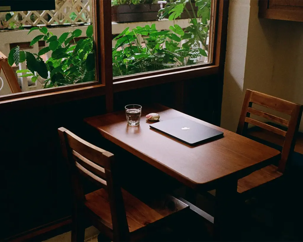 A laptop placed on a café table surrounded by a relaxed coffee shop setting, suggesting a remote work or study moment while enjoying the quiet and comfortable café environment.