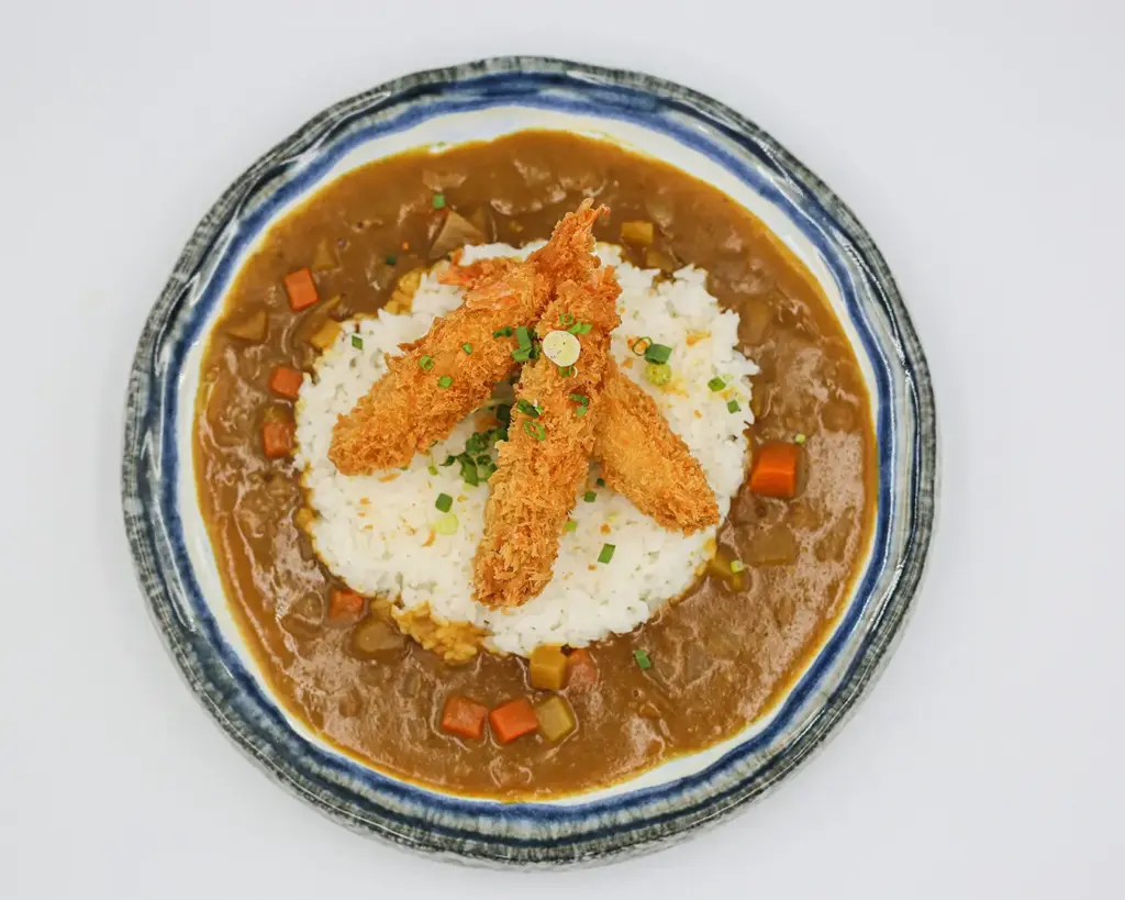 A comforting serving of Japanese curry with thick, rich curry sauce poured over steamed white rice, often accompanied by vegetables and tender meat.