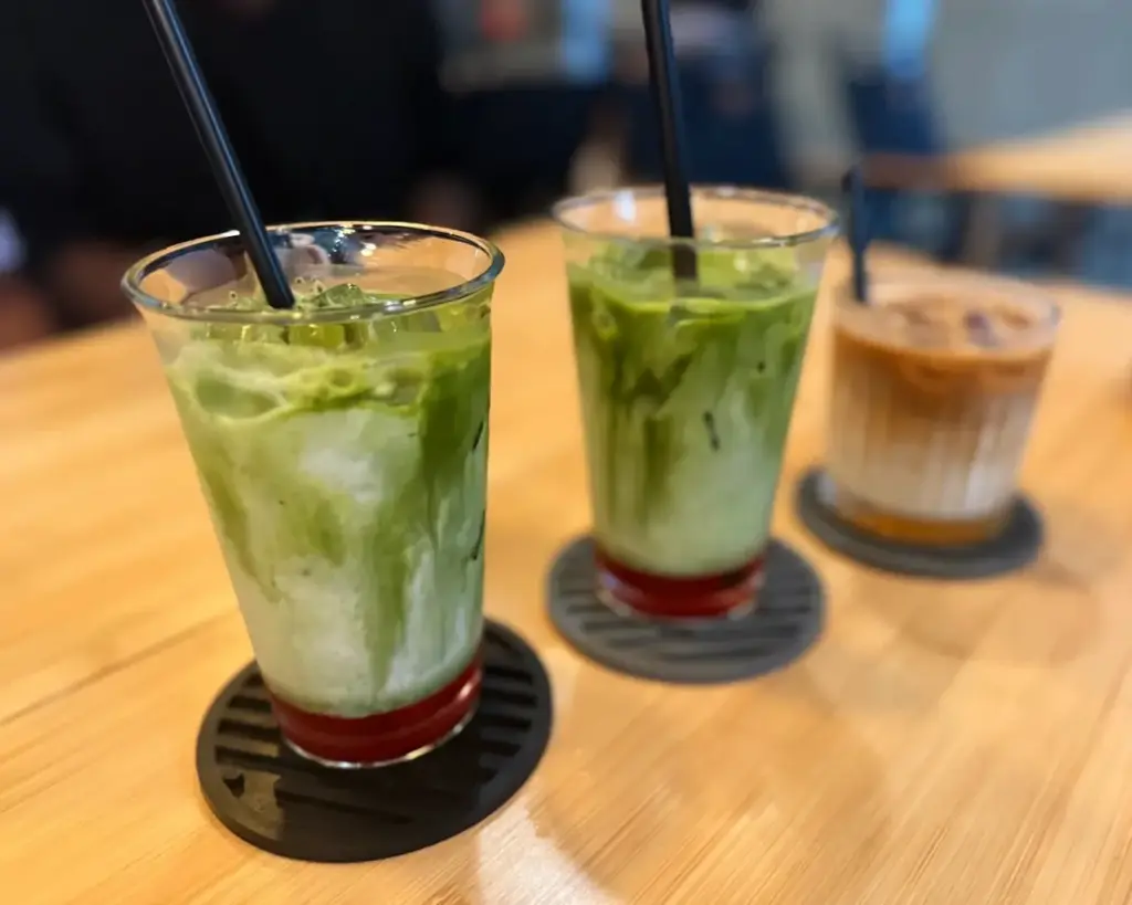 Two vibrant glasses of strawberry matcha layered with green matcha and pink strawberry milk sit beside a creamy coffee latte. The colourful drinks create an appealing contrast, making the table look refreshing and visually inviting.