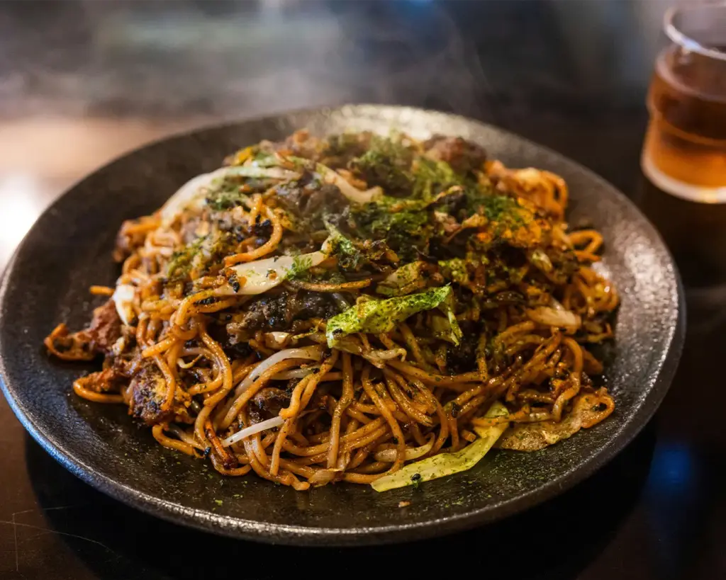 A plate of fried noodles served on a table beside a simple glass of water, highlighting a casual everyday meal.