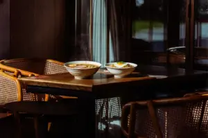Two steaming bowls of Japanese ramen and fried rice topped with a sunny-side-up egg on a rustic wooden table in a dimly lit, cozy restaurant.