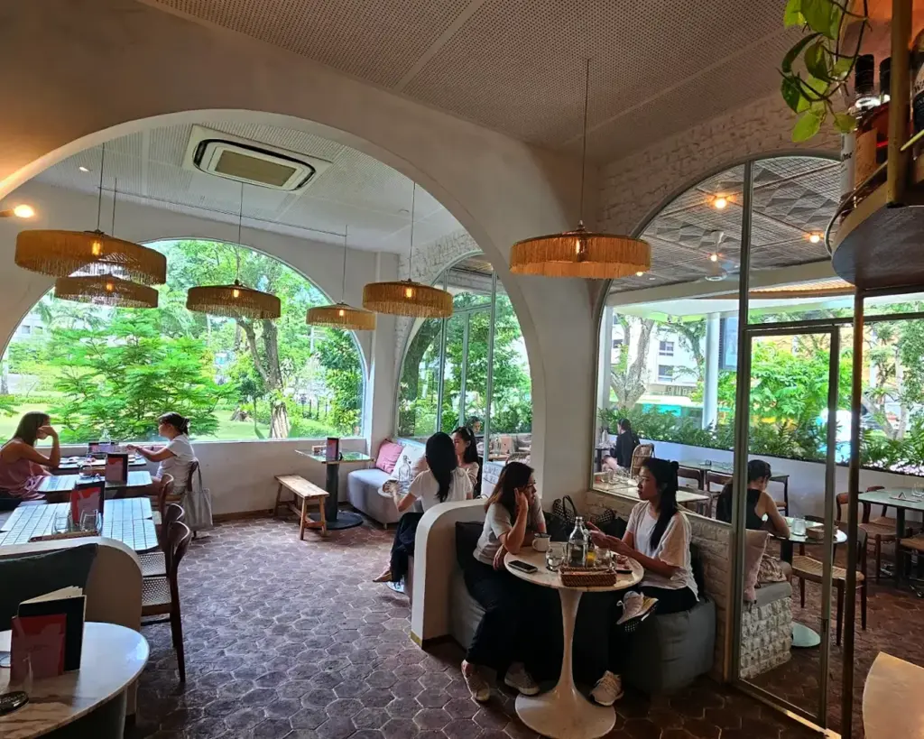 Modern cafe with arched windows, wicker lamps, and lush outdoor views. People enjoy casual conversations, creating a cozy, inviting atmosphere.